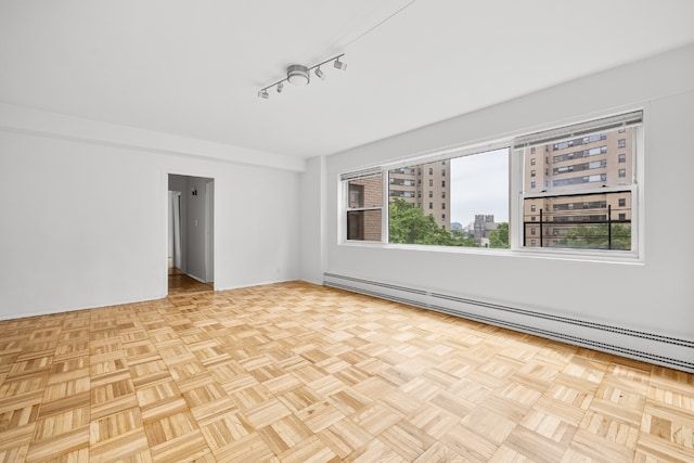 spare room featuring light parquet floors, a baseboard heating unit, and track lighting