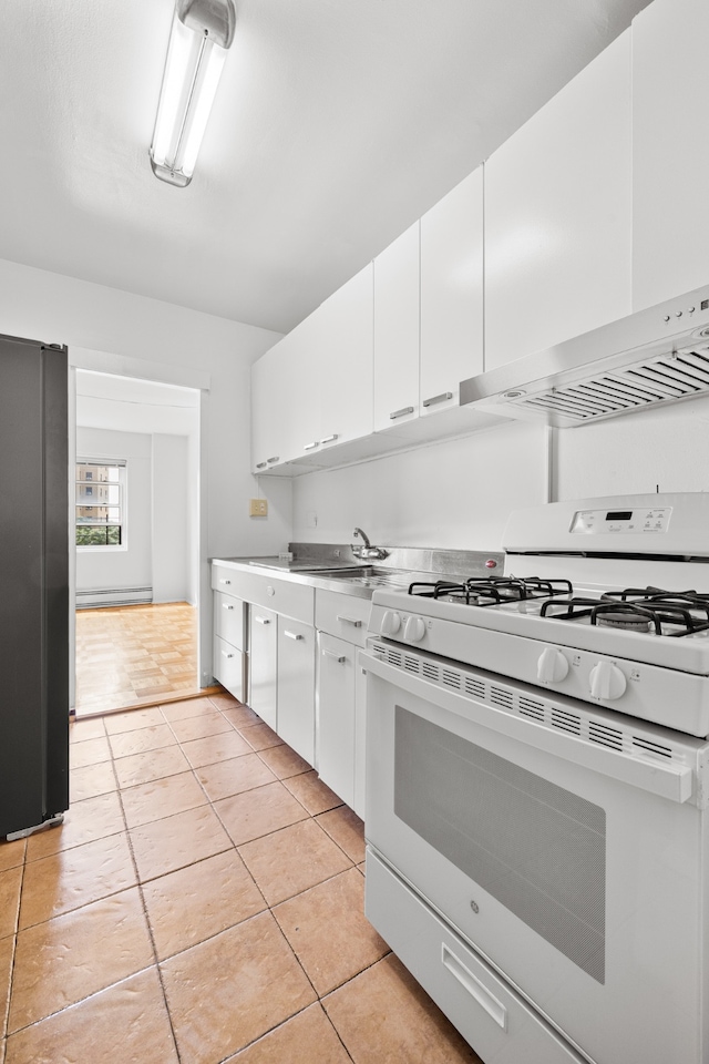 kitchen with range hood, white gas range oven, freestanding refrigerator, and white cabinets