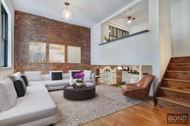 living room featuring hardwood / wood-style flooring, brick wall, and ceiling fan