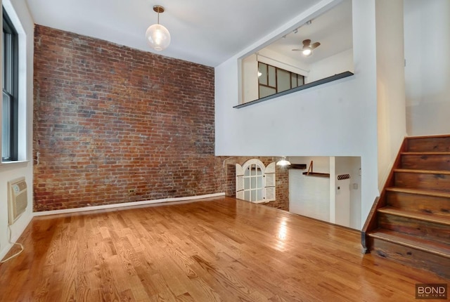 unfurnished living room with ceiling fan, wood-type flooring, and brick wall