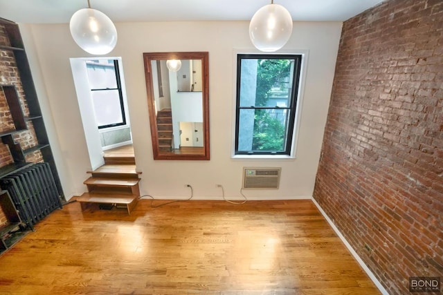 unfurnished room with a wall mounted AC, hardwood / wood-style flooring, brick wall, a fireplace, and radiator