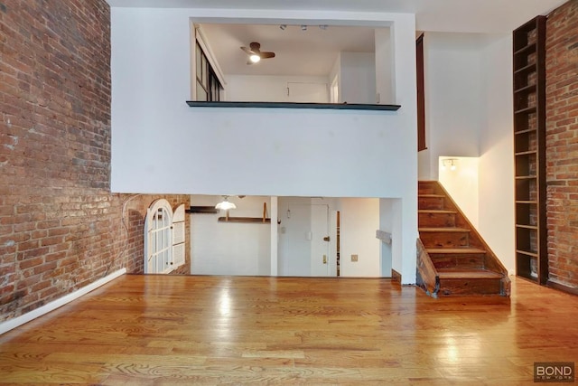 unfurnished living room with brick wall, a towering ceiling, hardwood / wood-style floors, and built in shelves