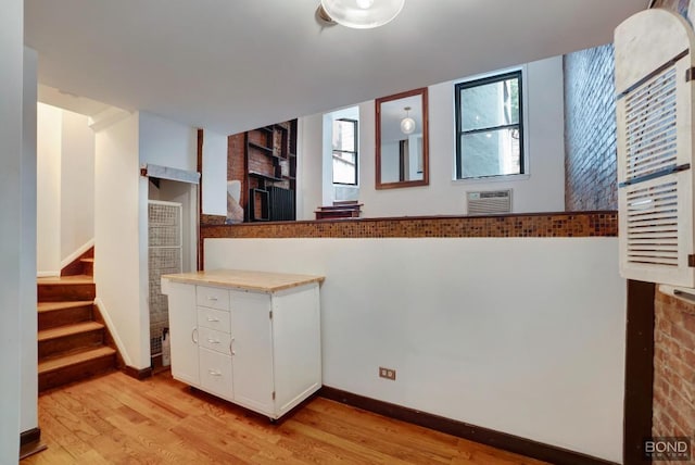 kitchen featuring light wood-type flooring, white cabinets, and an AC wall unit