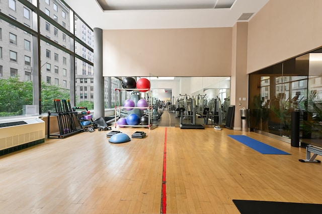 exercise room with radiator heating unit, a towering ceiling, and hardwood / wood-style floors