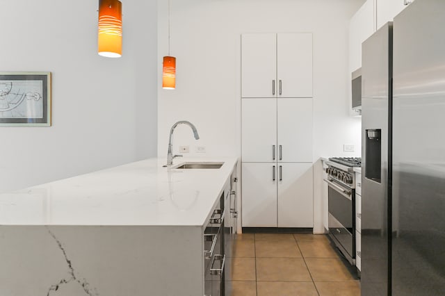 kitchen featuring white cabinets, appliances with stainless steel finishes, light stone countertops, pendant lighting, and a sink