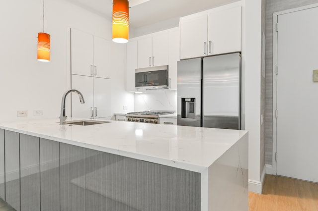 kitchen with stainless steel appliances, a peninsula, a sink, white cabinetry, and decorative light fixtures