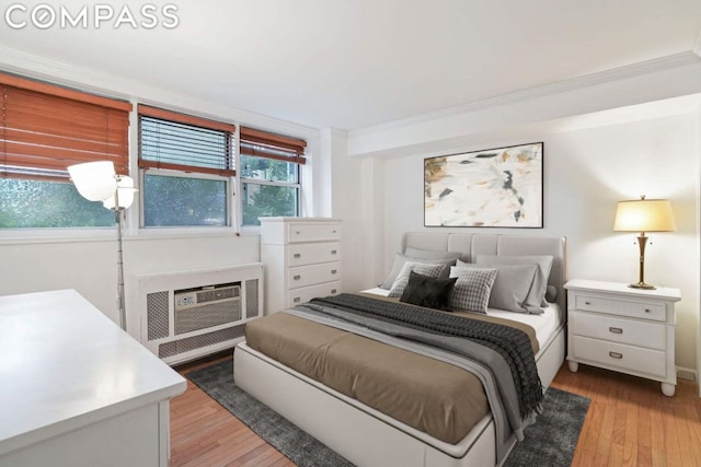 bedroom with ornamental molding, light hardwood / wood-style floors, an AC wall unit, and multiple windows