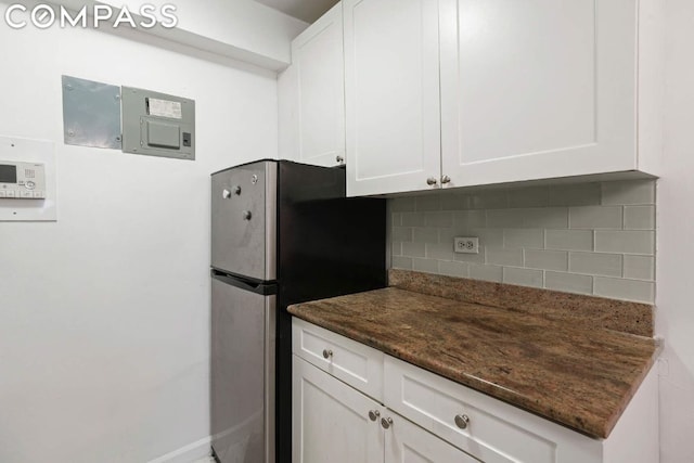 kitchen with white cabinetry, decorative backsplash, dark stone counters, and stainless steel refrigerator