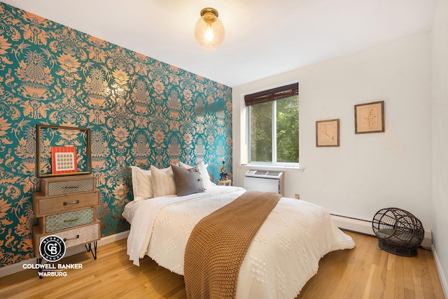 bedroom with a baseboard radiator, wood finished floors, a wall mounted air conditioner, and wallpapered walls