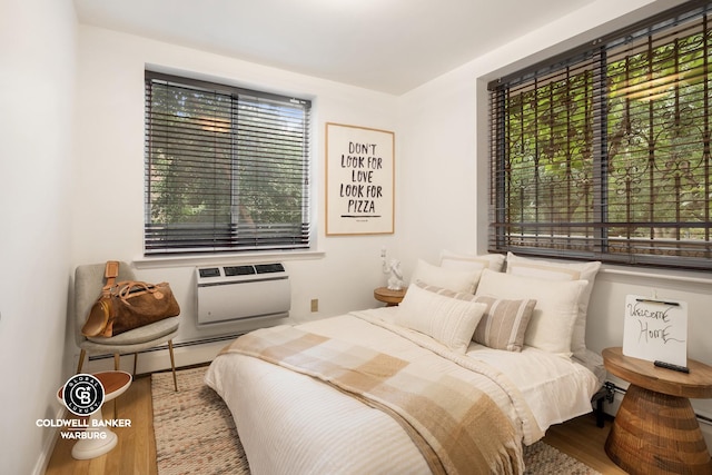 bedroom featuring an AC wall unit, baseboard heating, and wood finished floors