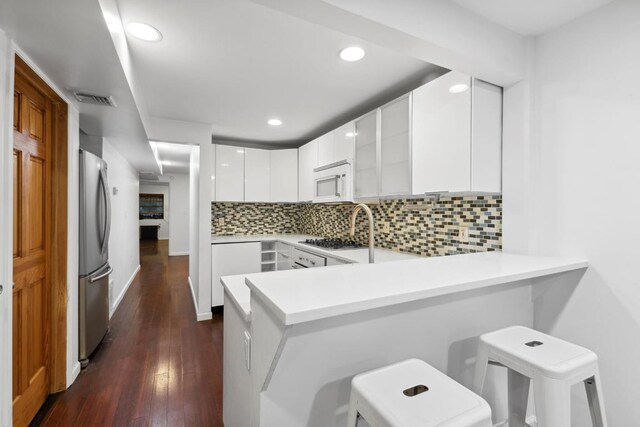 kitchen with tasteful backsplash, a kitchen breakfast bar, stainless steel appliances, white cabinetry, and kitchen peninsula