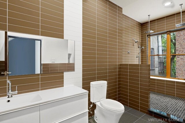 bathroom featuring tile patterned flooring, toilet, a tile shower, tile walls, and vanity