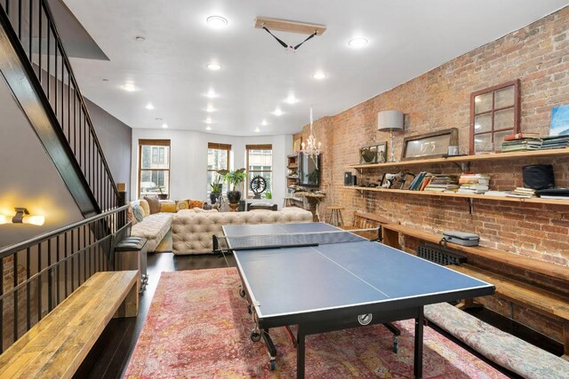 playroom featuring a chandelier, wood-type flooring, and brick wall