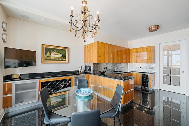 kitchen featuring tasteful backsplash, granite finish floor, hanging light fixtures, a chandelier, and beverage cooler