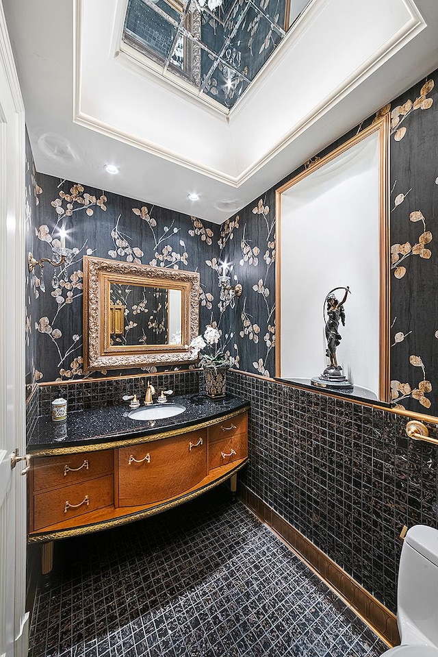bathroom featuring wallpapered walls, a wainscoted wall, vanity, toilet, and tile walls