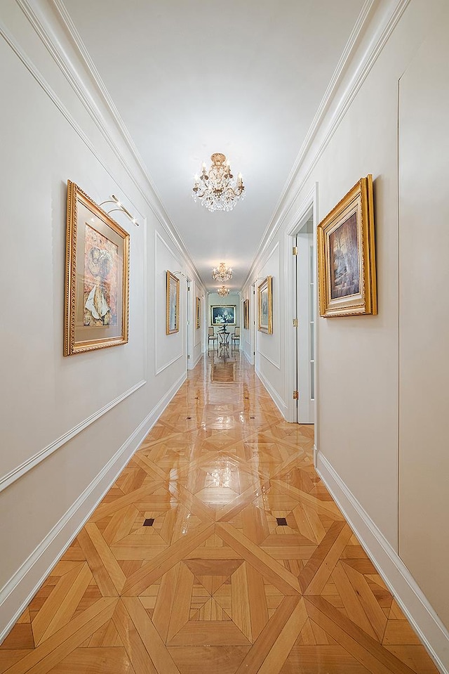 hall with an inviting chandelier, a decorative wall, baseboards, and ornamental molding