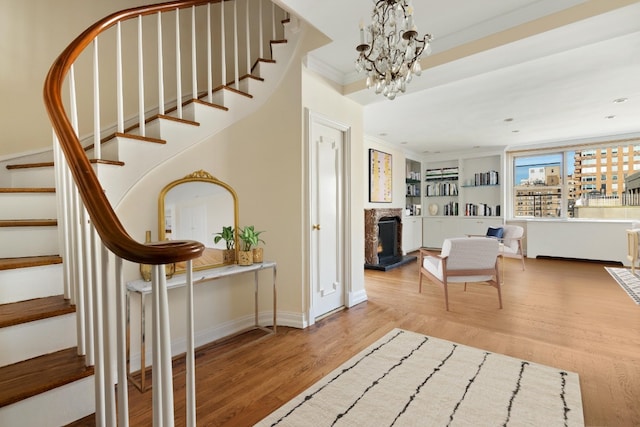 entrance foyer with stairs, a warm lit fireplace, wood finished floors, and crown molding