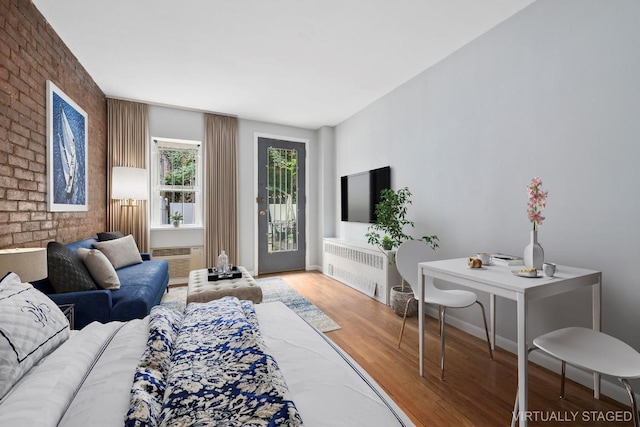 living room featuring radiator, brick wall, hardwood / wood-style flooring, and a wall mounted air conditioner