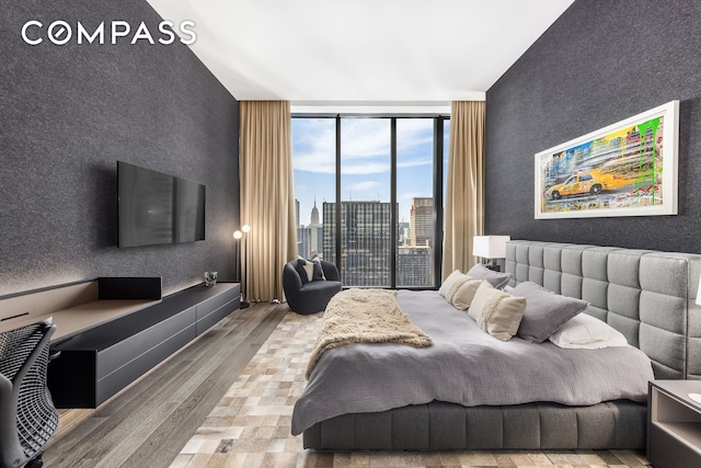 bedroom featuring an accent wall, wood finished floors, floor to ceiling windows, and access to exterior