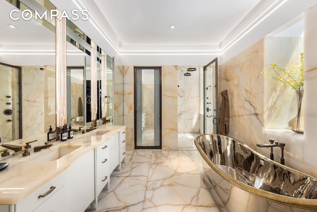 full bathroom with marble finish floor, a marble finish shower, double vanity, a soaking tub, and stone wall