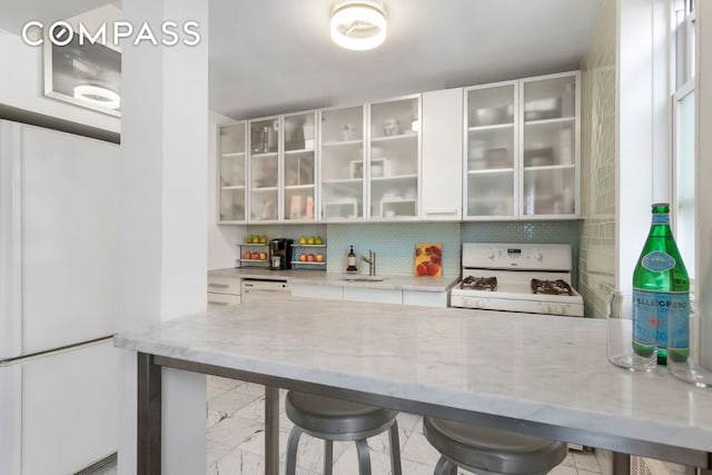 bar featuring sink, light stone countertops, white cabinets, white range with gas cooktop, and decorative backsplash