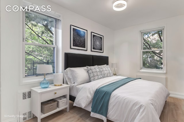 bedroom featuring multiple windows, radiator, and light hardwood / wood-style floors