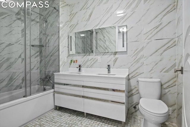 full bathroom featuring toilet, bath / shower combo with glass door, tile walls, vanity, and tile patterned floors