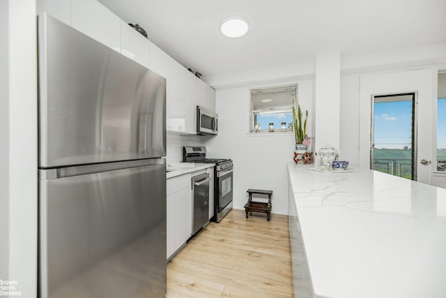 kitchen featuring tasteful backsplash, white cabinetry, light stone counters, stainless steel appliances, and light hardwood / wood-style flooring