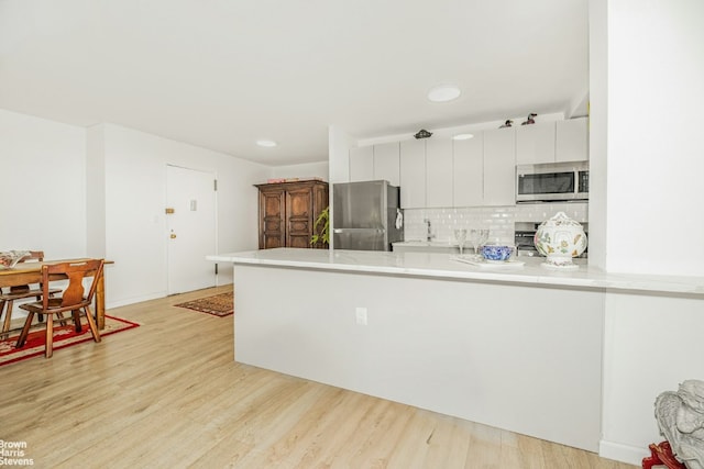 kitchen with appliances with stainless steel finishes, white cabinetry, backsplash, light hardwood / wood-style floors, and kitchen peninsula