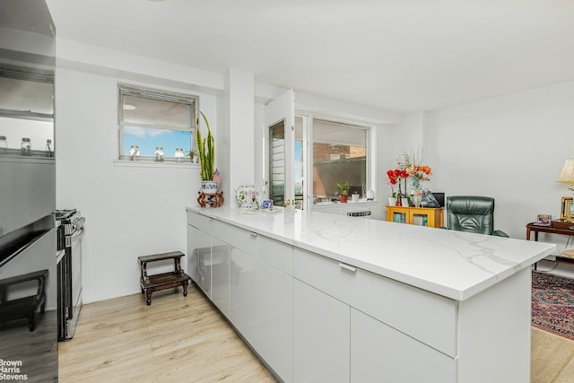 kitchen with white cabinetry, stainless steel range, light hardwood / wood-style floors, kitchen peninsula, and light stone countertops