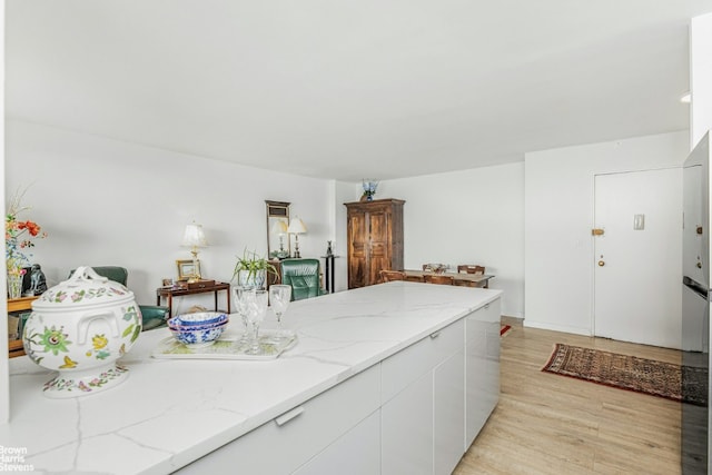 kitchen with light stone countertops, light wood-type flooring, and white cabinets