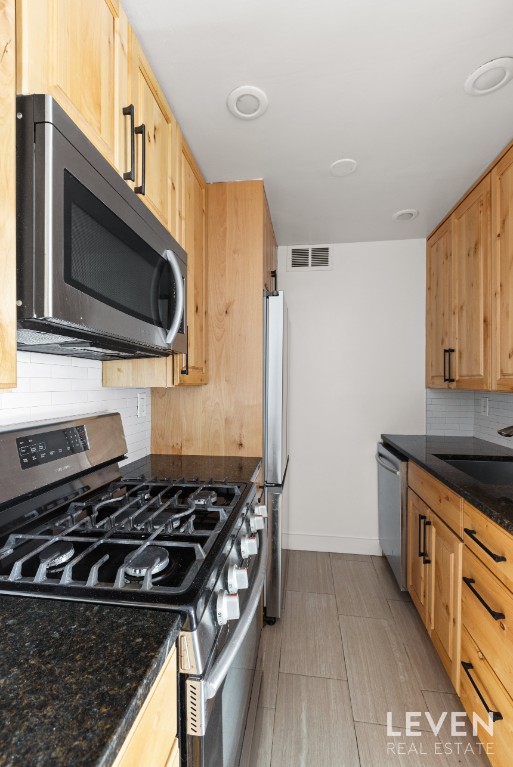 kitchen with stainless steel appliances, tasteful backsplash, sink, and dark stone counters