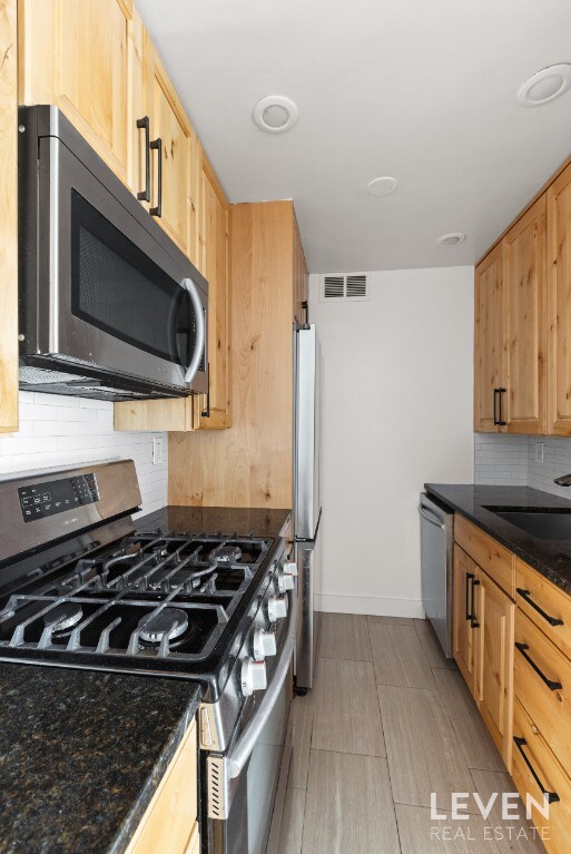 kitchen with stainless steel appliances, decorative backsplash, baseboards, a sink, and dark stone countertops