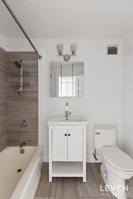 bathroom with toilet, shower / bath combination, vanity, wood finished floors, and baseboards