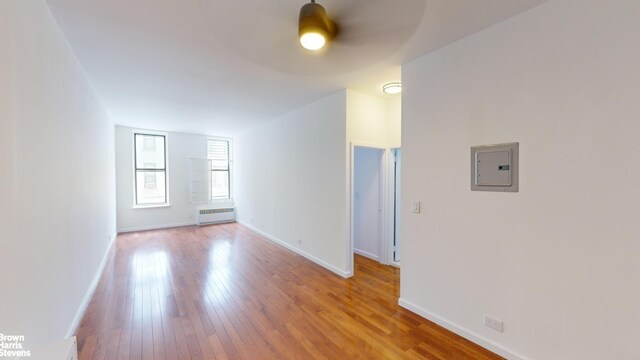 empty room featuring ceiling fan, electric panel, radiator, and light hardwood / wood-style flooring