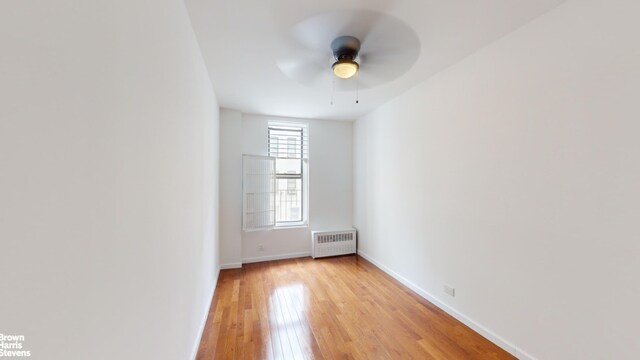 unfurnished room with ceiling fan, radiator heating unit, and light hardwood / wood-style flooring