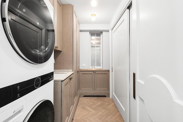 laundry room with stacked washer and clothes dryer, light parquet floors, and cabinets