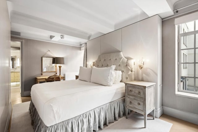 bedroom with beam ceiling, ensuite bathroom, and light hardwood / wood-style floors