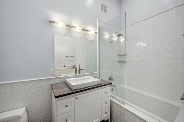 full bathroom with tiled shower / bath combo, vanity, tile walls, and toilet