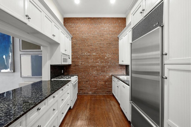 kitchen featuring white appliances, dark stone counters, white cabinets, and brick wall