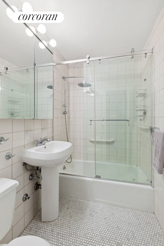 bathroom featuring combined bath / shower with glass door, toilet, and tile walls