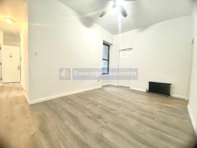 unfurnished room with hardwood / wood-style flooring, ceiling fan, and radiator heating unit