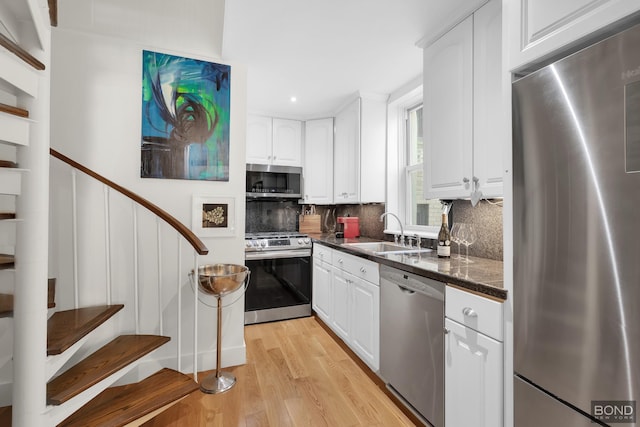 kitchen with stainless steel appliances, dark countertops, a sink, and white cabinets