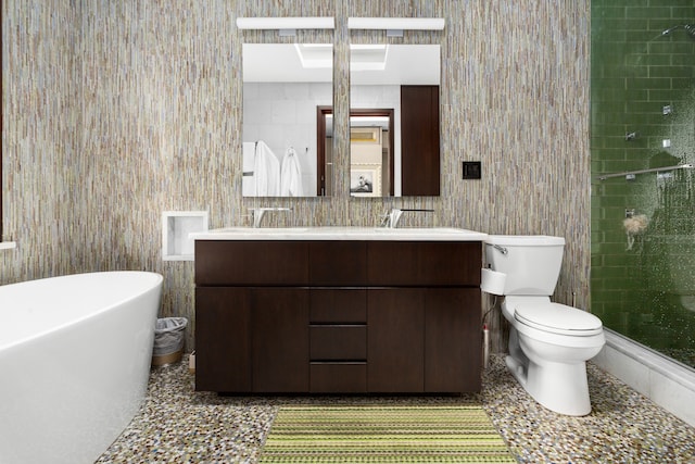 bathroom featuring toilet, tile walls, a freestanding bath, double vanity, and a stall shower