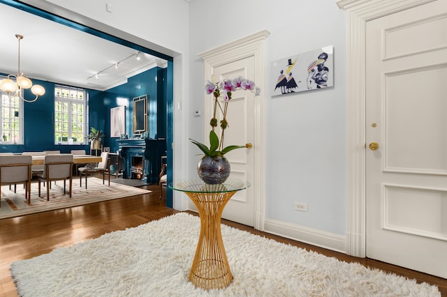 entrance foyer featuring a warm lit fireplace, baseboards, wood finished floors, a chandelier, and track lighting