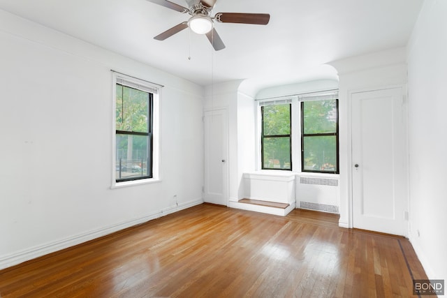 empty room with a healthy amount of sunlight, radiator heating unit, ceiling fan, and hardwood / wood-style floors