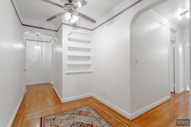 corridor featuring built in features, arched walkways, baseboards, and wood finished floors