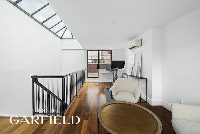 interior space with a skylight, baseboards, an AC wall unit, and wood finished floors