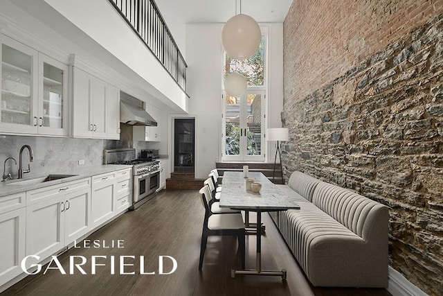 kitchen with range with two ovens, dark wood-style flooring, a sink, white cabinetry, and wall chimney exhaust hood