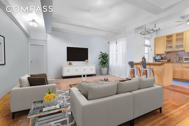 living room featuring beamed ceiling, light wood-type flooring, and a ceiling fan